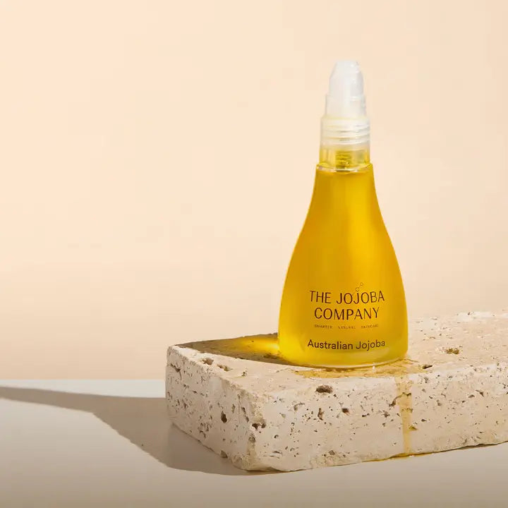 Bottle of The Jojoba Company Australian Jojoba oil on a stone surface with a beige background