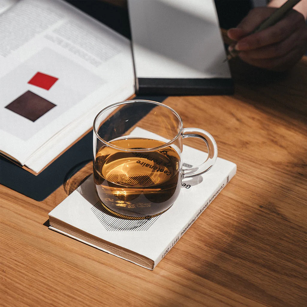 Clear glass mug with tea on a book on a wooden table